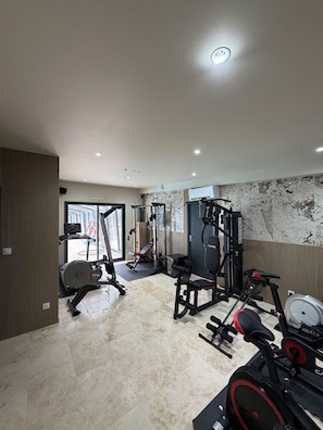 Academia com equipamentos de exercícios, um banco e uma parede com padrão semelhante ao mármore.
