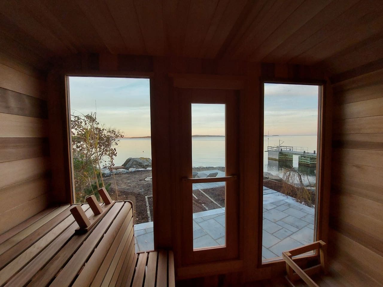 Eine Holzdiele mit einer Bank und Blick auf ein Gewässer durch große Fenster.