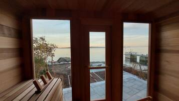 Eine Holzdiele mit einer Bank und Blick auf ein Gewässer durch große Fenster.