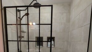 Ducha envuelta en vidrio con pared de azulejos, cabezal de ducha manual y grifo empotrado.