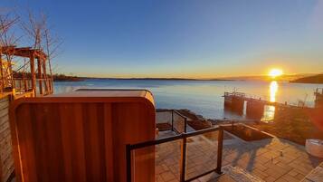 Ein Haus am Wasser mit Whirlpool, einer Holzterrasse und Blick auf den Sonnenuntergang über dem Wasser.