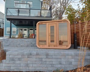 Una casa moderna con estructura de dos pisos, un patio cubierto y una terraza de madera con puertas de vidrio.