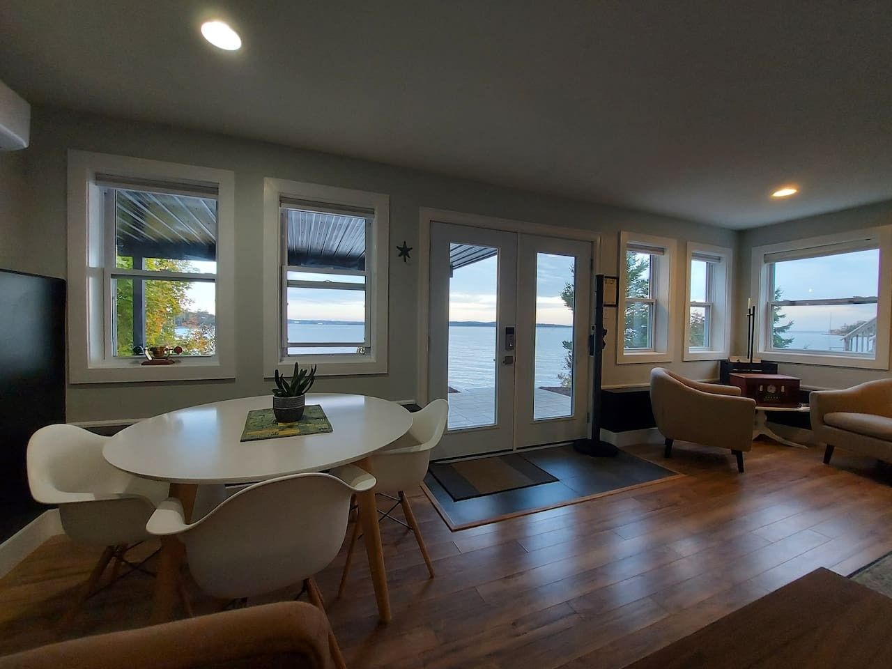 Ein modernes Wohnzimmer mit rundem Tisch und Stühlen, einer Couch und großen Fenstern mit Blick auf das Wasser.