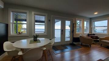 Ein modernes Wohnzimmer mit rundem Tisch und Stühlen, einer Couch und großen Fenstern mit Blick auf das Wasser.