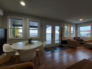 Ein modernes Wohnzimmer mit rundem Tisch und Stühlen, einer Couch und großen Fenstern mit Blick auf das Wasser.