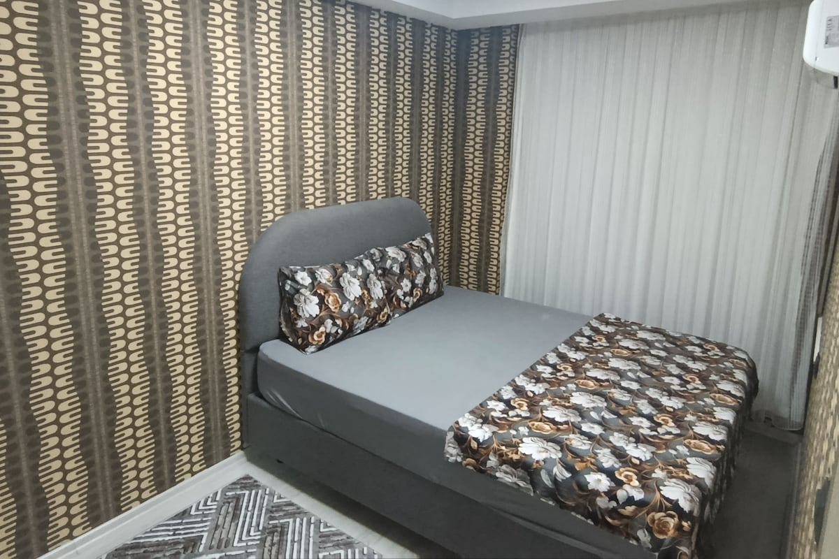 Un dormitorio con cama, cortinas y una colcha estampada.