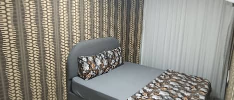 Un dormitorio con cama, cortinas y una colcha estampada.