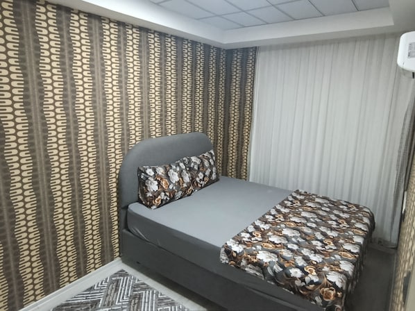A bedroom with a bed, curtains, and a patterned bedspread.