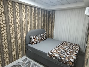 Un dormitorio con cama, cortinas y una colcha estampada.