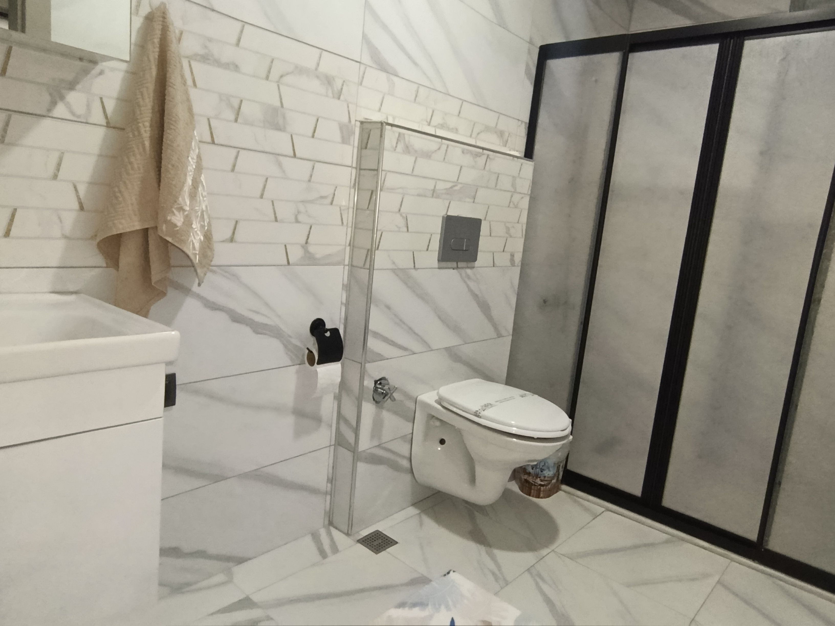 A bathroom with a white toilet, a glass shower enclosure, and a marble-patterned wall.