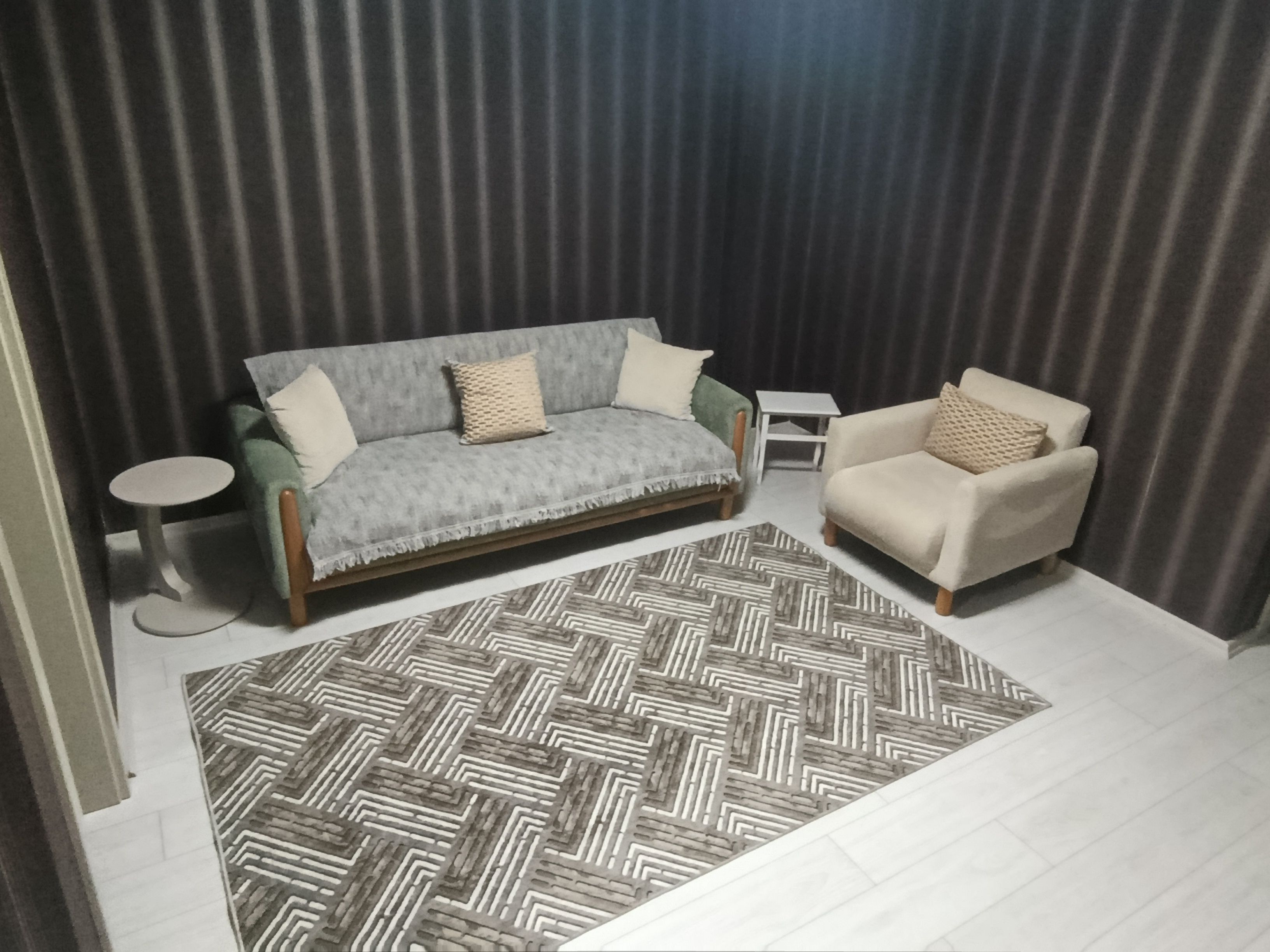 A living room with a sofa, a chair, a small table, and a patterned rug.
