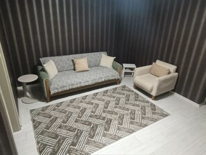 A living room with a sofa, a chair, a small table, and a patterned rug. - Alp Apart Otel (Aksaray)