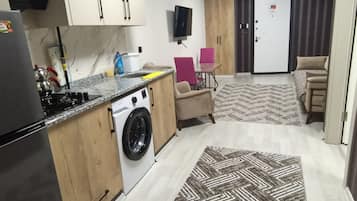 A compact kitchen with a washing machine, a stove, and a sink. There is a patterned rug on the floor and a door with a sign.