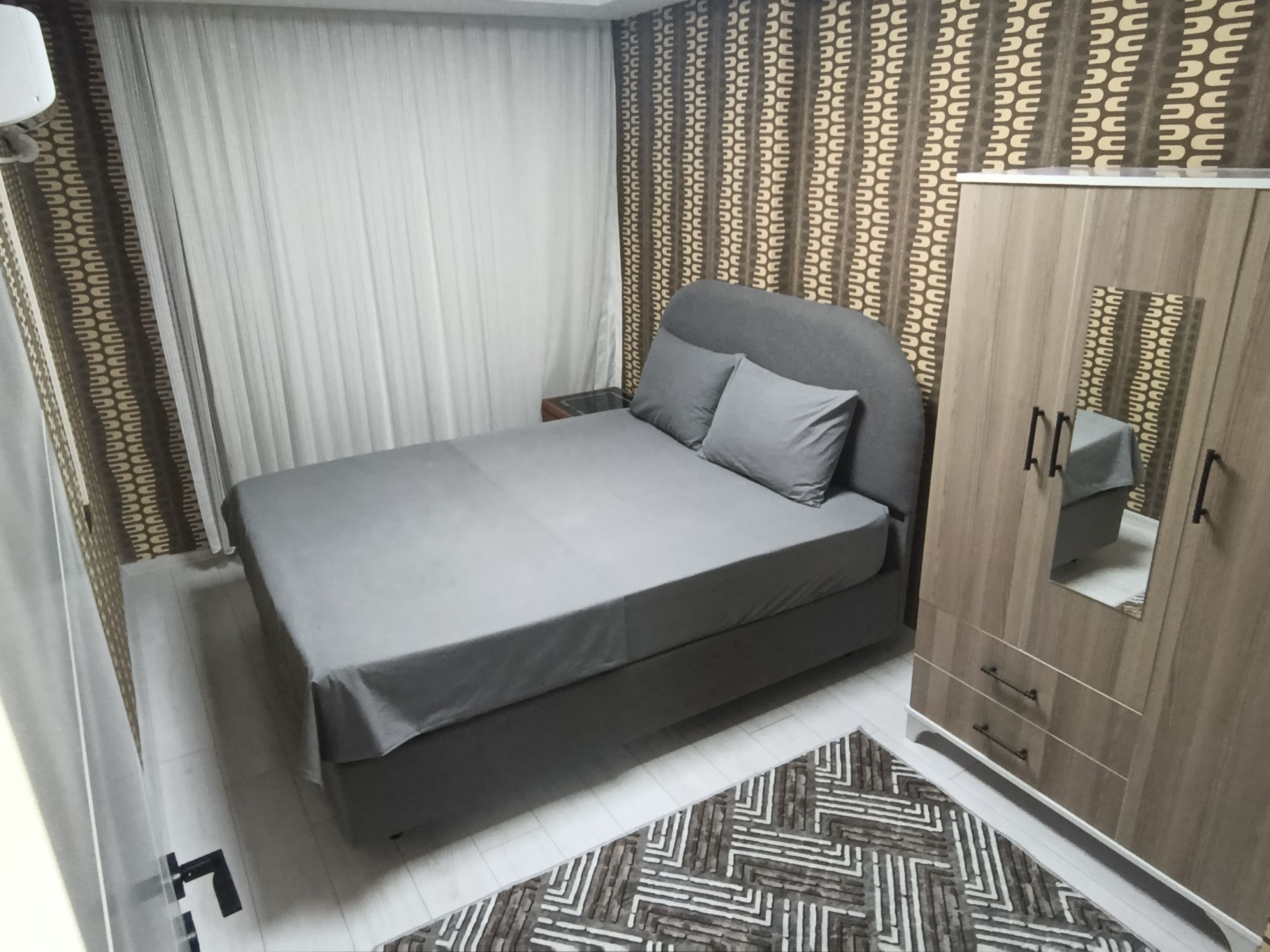 Un dormitorio con cama, armario y una alfombra estampada.
