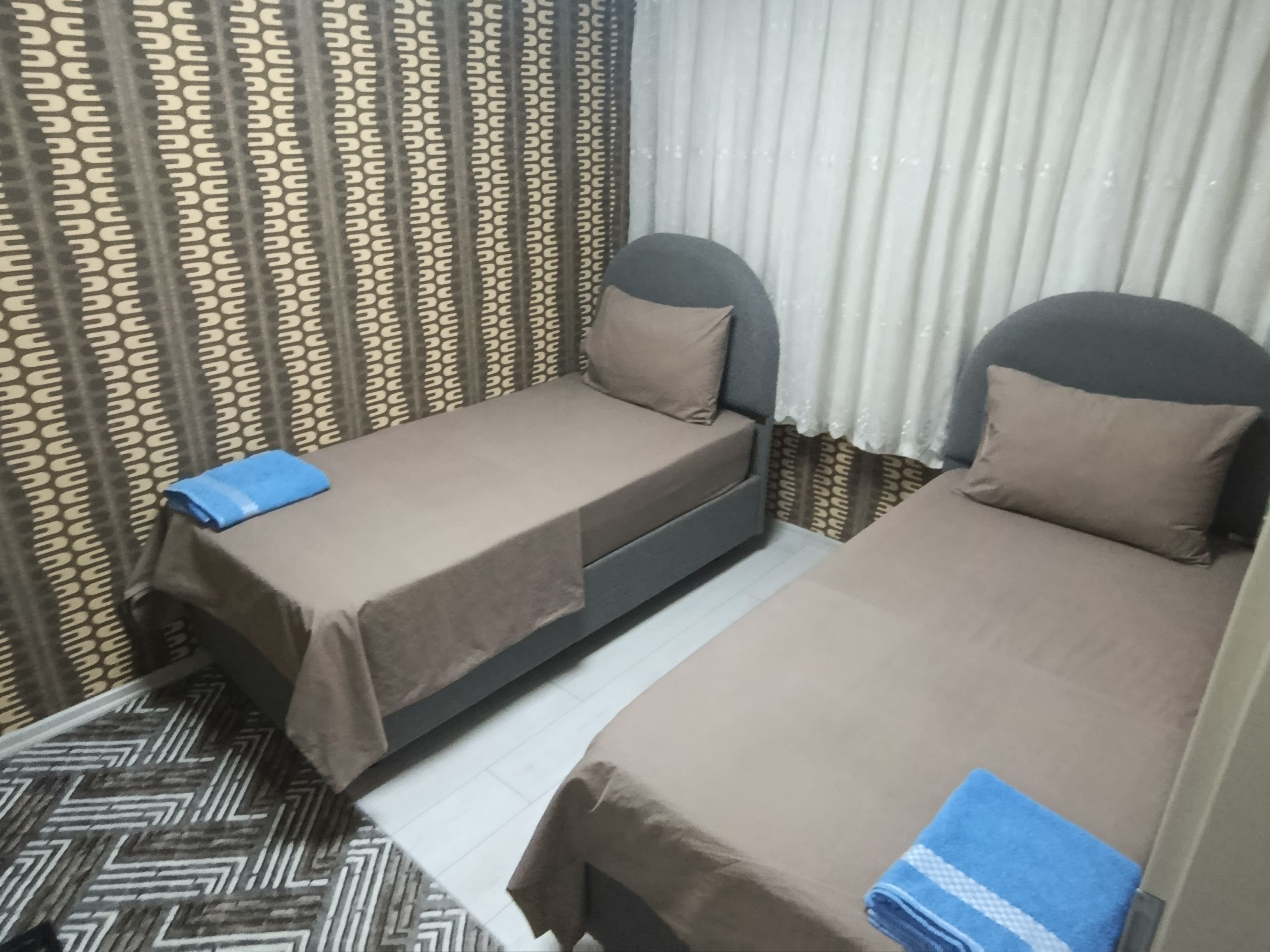 A room with two beds, a patterned curtain, and a patterned floor.