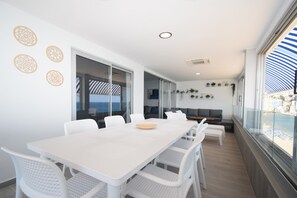A modern dining area with a white table and chairs, a view of the sea through large windows, and a balcony with a striped awning. - TOR Serena 15C in Benidorm (Benidorm)