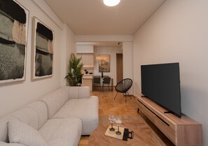 Ein Wohnzimmer mit einer Couch, einem Flachbildfernseher, einem Couchtisch mit Gläsern und einem Essbereich mit Stühlen und einem Tisch.
