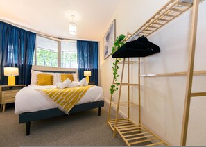 A neatly arranged hotel room with a bed, two bedside tables with lamps, a wooden ladder shelf, and a window with curtains. - Spacious 4BR Apartment in Notting Hill (London)