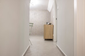 A hallway with a wooden cabinet, a chair, and a wall with a geometric pattern. - Room 'Soleil Rooms - Salvia' (Catania)