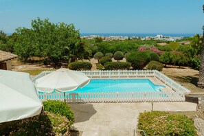 A swimming pool with a white fence, surrounded by greenery and a view of the sea. - Olinda Seaview Villa (Paralimni)