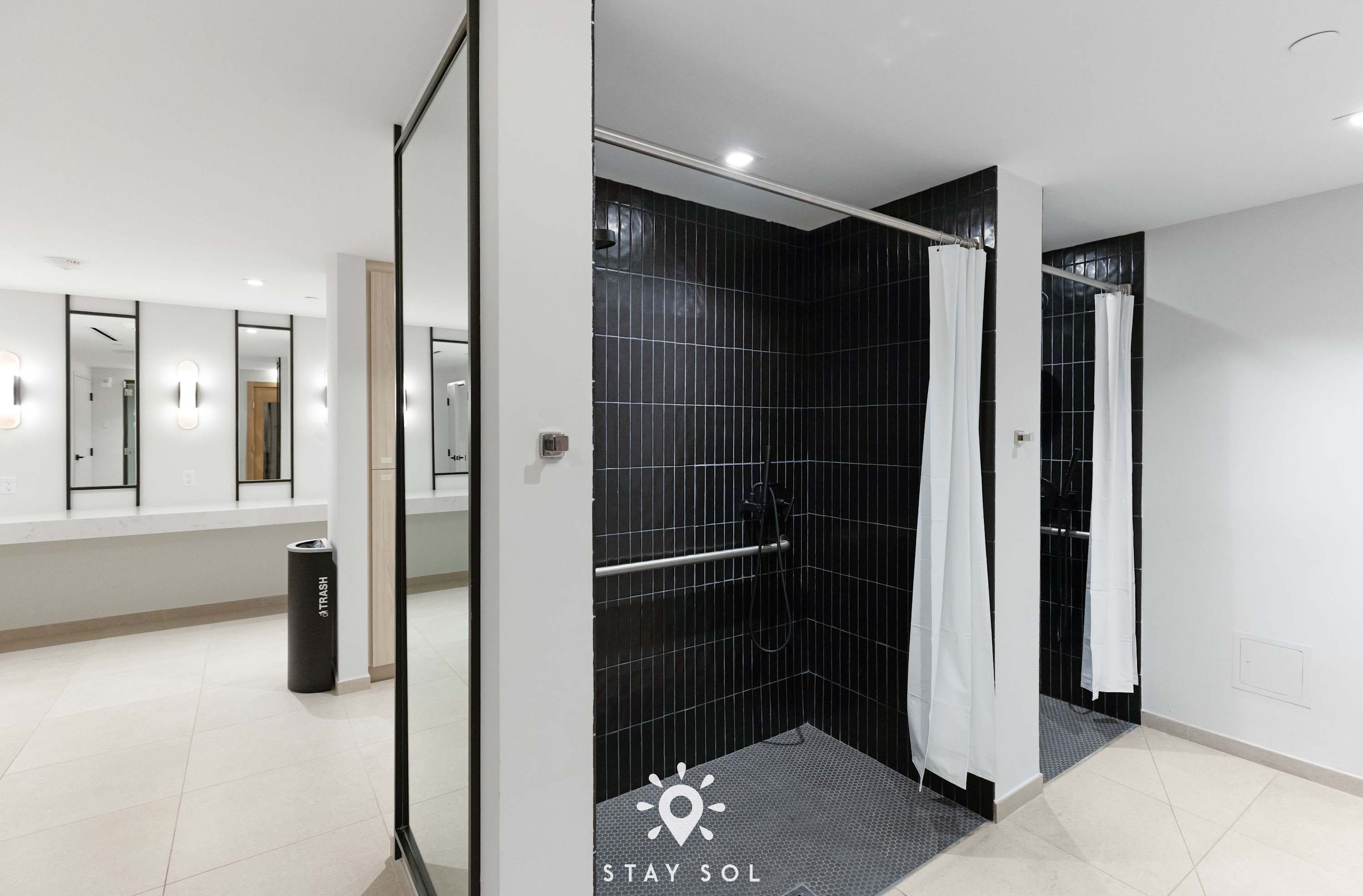 A modern bathroom with a shower, a toilet, and a trash bin.