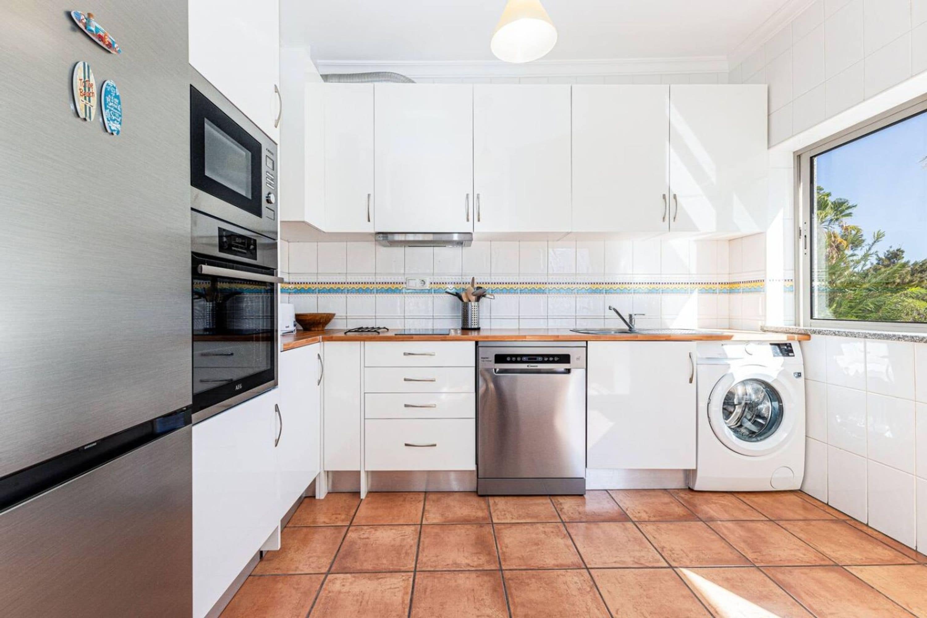 Eine moderne Küche mit weißen Schränken, einem Edelstahl-Kühlschrank, einem Backofen, einem Geschirrspüler und einer Waschmaschine.