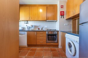 A compact kitchen with wooden cabinets, a built-in oven, a washing machine, and a coffee maker. - Marina Park Outdoor Pool Garage Balcony (Lagos)