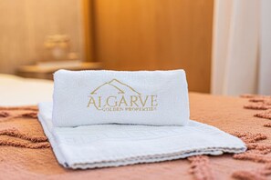Ein ordentlich gefaltetes weißes Handtuch mit der Stickerei 'ALGARVE GOLDEN PROPERTIES' auf einer strukturierten Oberfläche.
