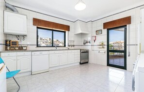 Eine moderne Küche mit weißen Schränken, einem Geschirrspüler, einem Backofen und einem großen Fenster mit Blick auf die Stadt.