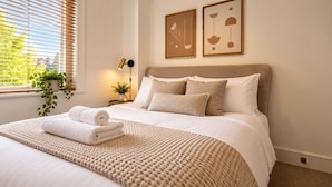 Una cama bien hecha con una toalla blanca enrollada, un plaid beige texturizado y dos almohadas.
