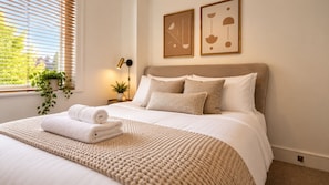 Una cama bien hecha con una toalla blanca enrollada, un plaid beige texturizado y dos almohadas.