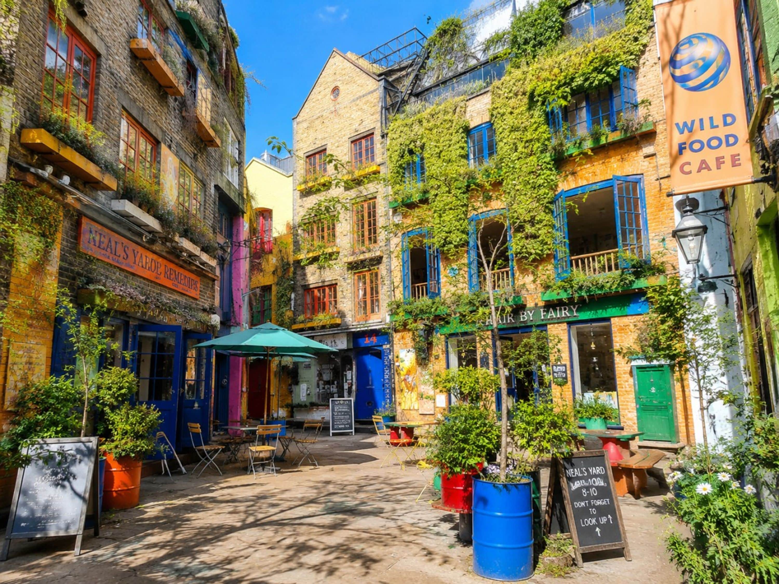A narrow street with buildings on either side, outdoor seating, and a sign for 'Wild Food Cafe'.