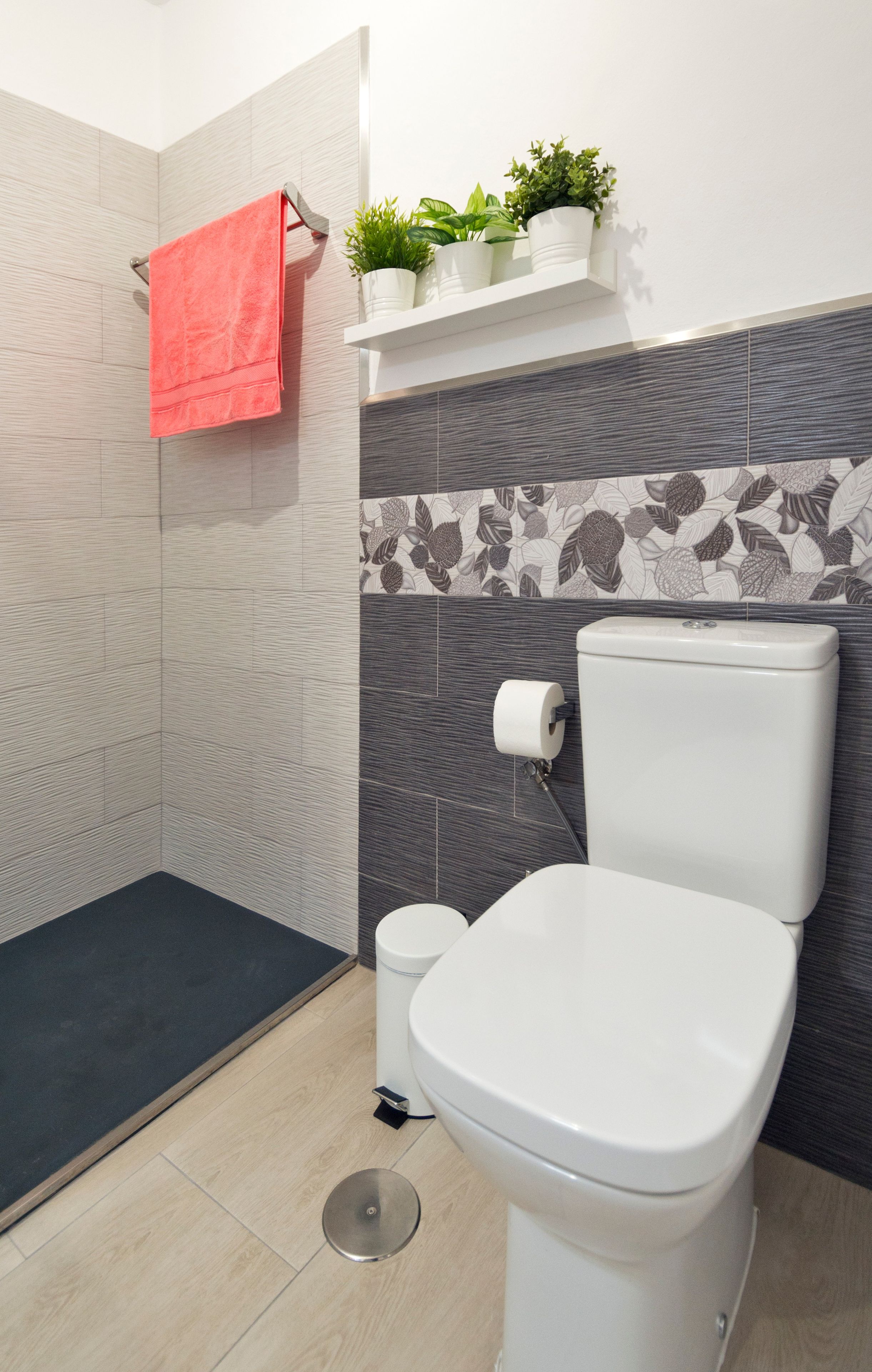 Een moderne badkamer met een toilet, een douchegedeelte en een klein plankje met planten.
