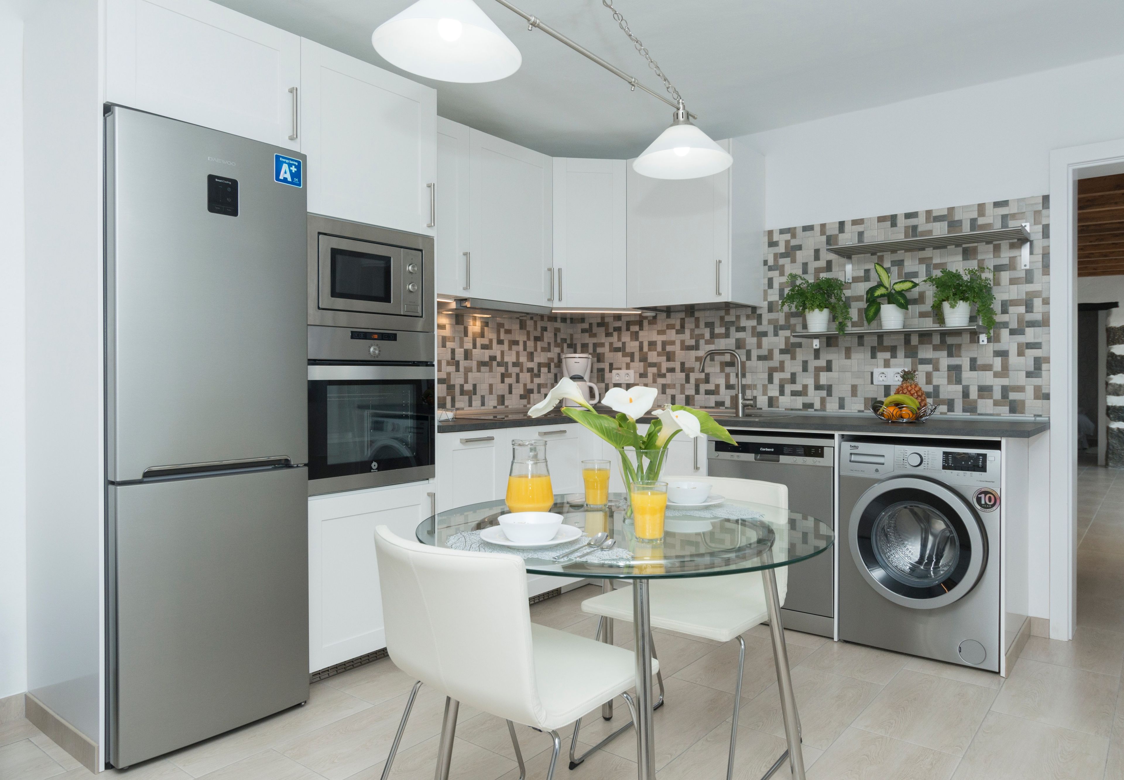 Una cocina moderna con electrodomésticos de acero inoxidable, una mesa de comedor de vidrio y una lavadora integrada.