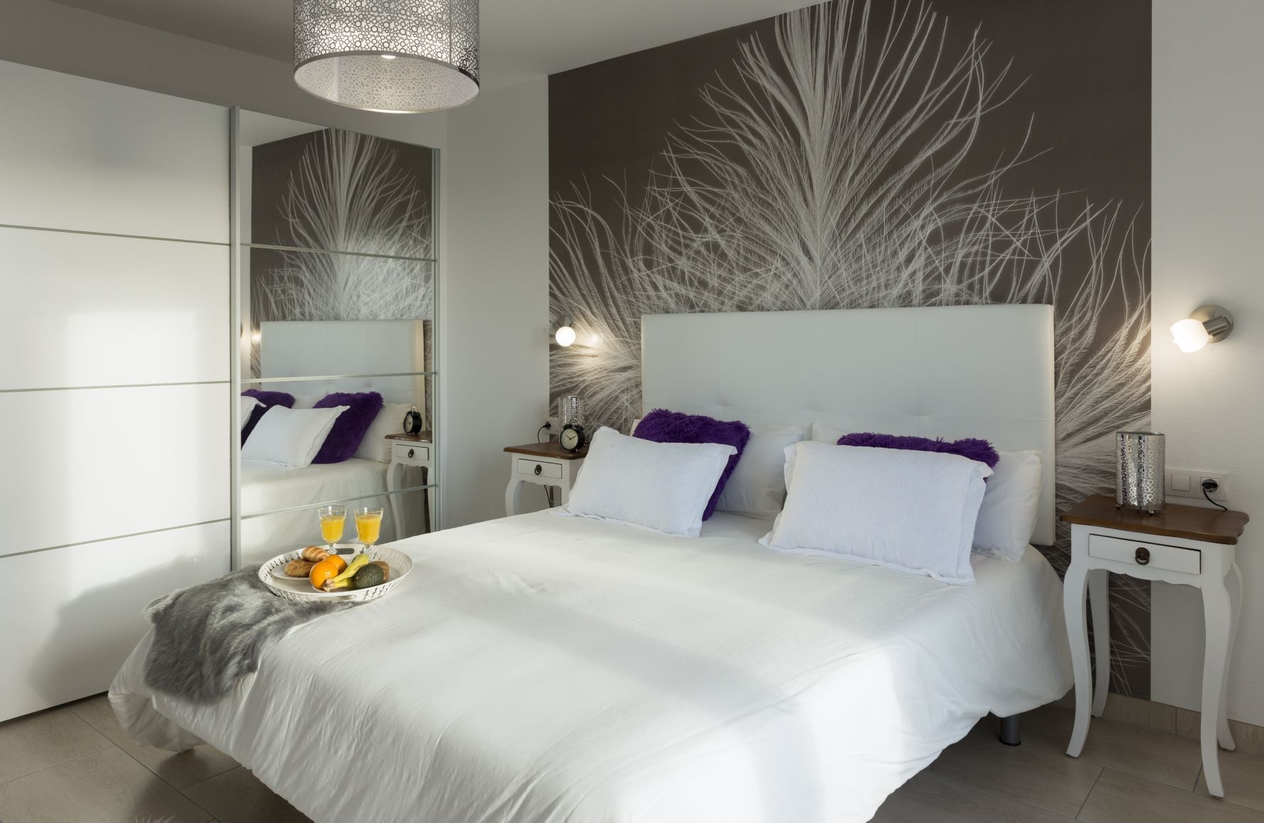 Une chambre à coucher moderne avec un grand lit, des tables de chevet, un miroir et une œuvre d’art murale.
