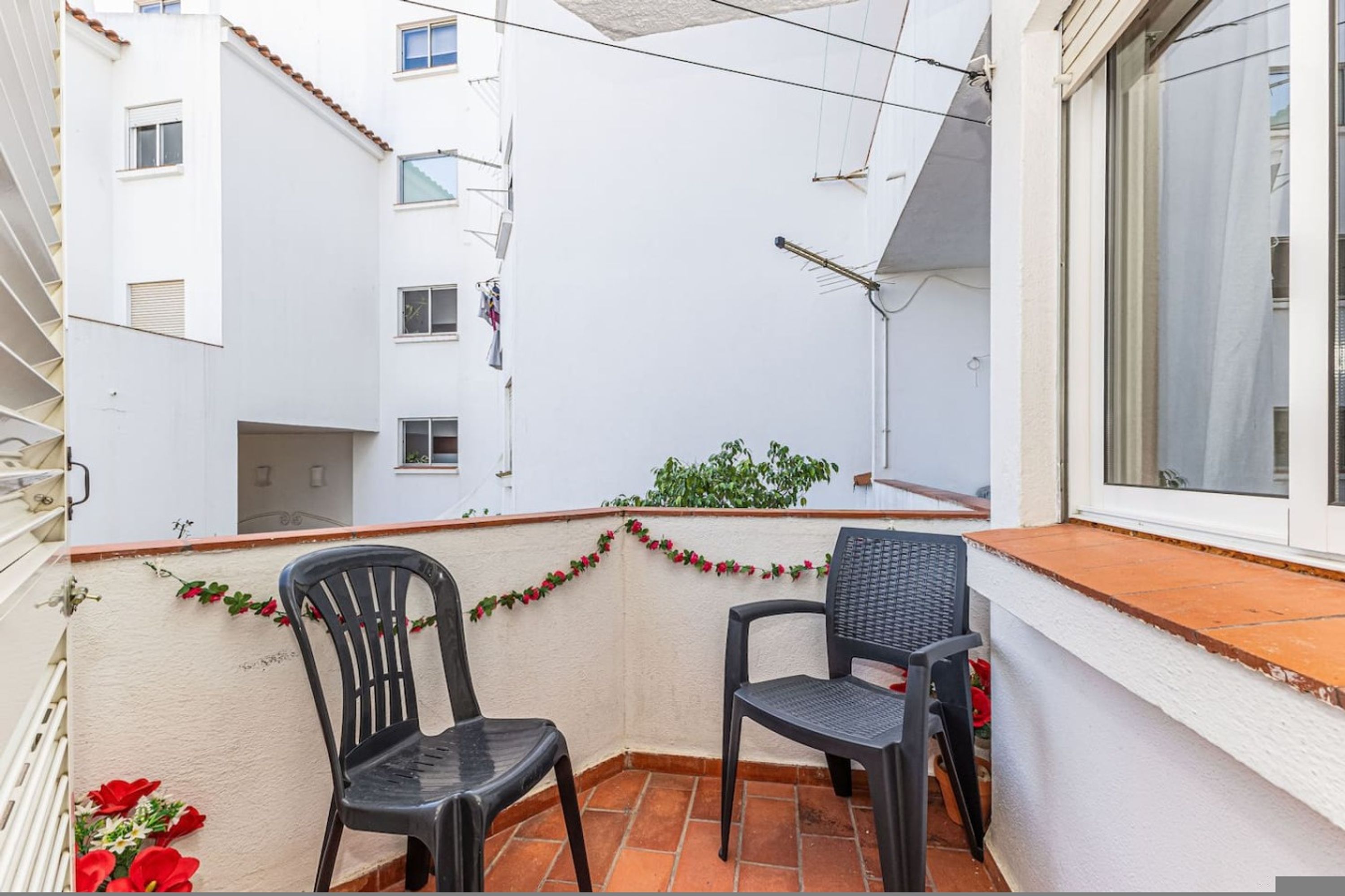 Un balcón con dos sillas, una ventana y vistas a un edificio blanco.