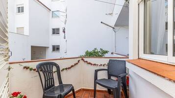 Un balcón con dos sillas, una ventana y vistas a un edificio blanco.