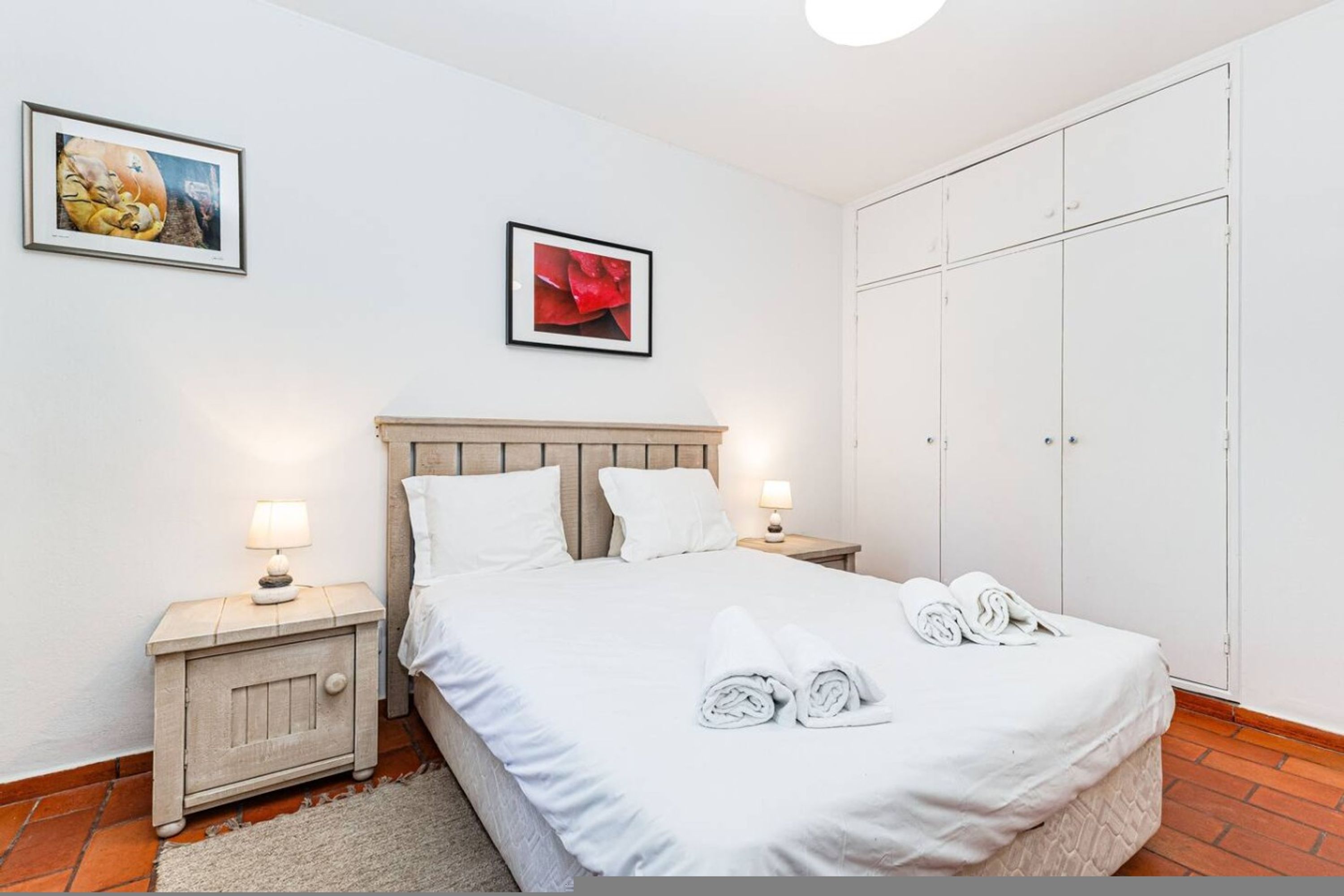 Um quarto com uma cama, duas mesas de cabeceira, um guarda-roupa e duas imagens emolduradas na parede.