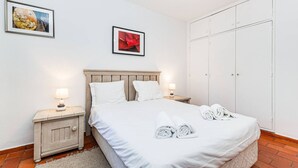 Een slaapkamer met een bed, twee nachtkastjes, een garderobe en twee ingelijste foto's aan de muur.