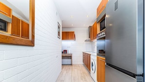 Eine schmale Küche mit weißen Ziegelwänden, Holzschränken und einem Edelstahl-Kühlschrank.