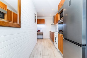 A narrow kitchen with white brick walls, wooden cabinets, and a stainless steel refrigerator. - Peaceful Panorama Apartment in Central Lagos (Lagos)