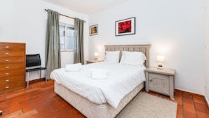 Ein Hotelzimmer mit einem Bett, zwei Nachttischen, einem Sessel, einem Schminktisch und einem Fenster mit Vorhängen.