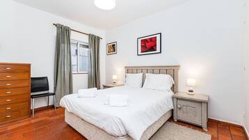 A hotel room with a bed, two bedside tables, a chair, a dresser, and a window with curtains.