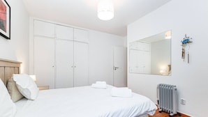 Ein Schlafzimmer mit einem Bett, weißen Vorhängen, einem Heizkörper und einem Spiegel an der Wand.