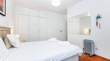 A bedroom with a bed, white curtains, a radiator, and a mirror on the wall.