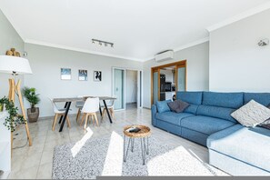 A modern living room with a blue sofa, dining area with chairs, and a kitchen in the background. - Varandas House Pool Near Meia Praia (Lagos)