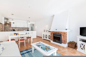 Un salon moderne avec une cheminée, un coin repas avec des chaises et une cuisine avec des meubles blancs.