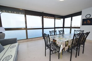 Ein Essbereich mit Tisch und Stühlen, große Fenster mit Meerblick und einer Uhr an der Wand.
