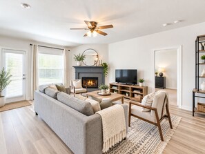 A modern living room with a fireplace, a television, and a ceiling fan. - Perfect 3-bedroom house with AC in enchanting McKinney (McKinney)