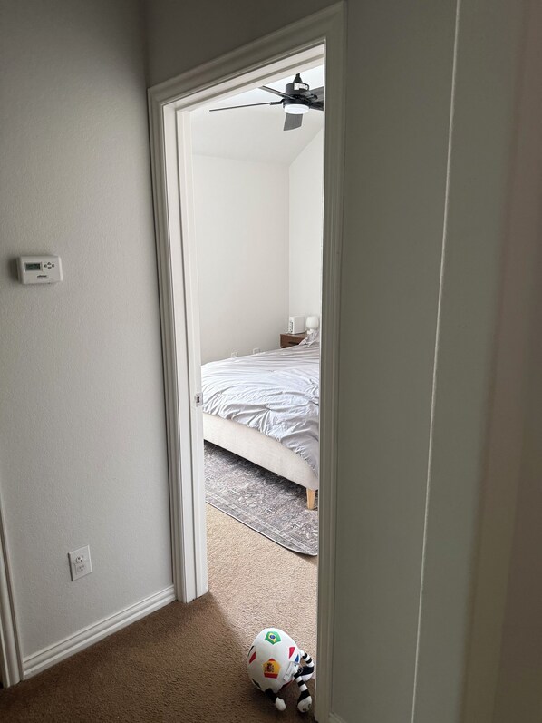 Ein Schlafzimmer mit einem Bett, einem Deckenventilator und einem an der Wand befestigten Thermostat.